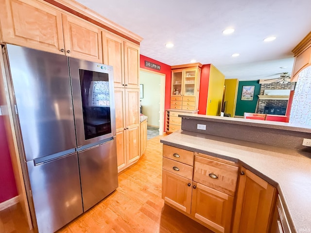 kitchen featuring light wood-style floors, a fireplace, recessed lighting, glass insert cabinets, and light brown cabinets