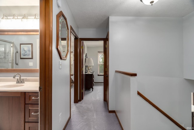 hall with a sink, an upstairs landing, carpet floors, and a textured ceiling