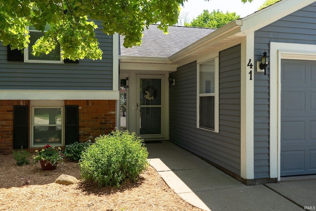 property entrance featuring brick siding, roof with shingles, and an attached garage