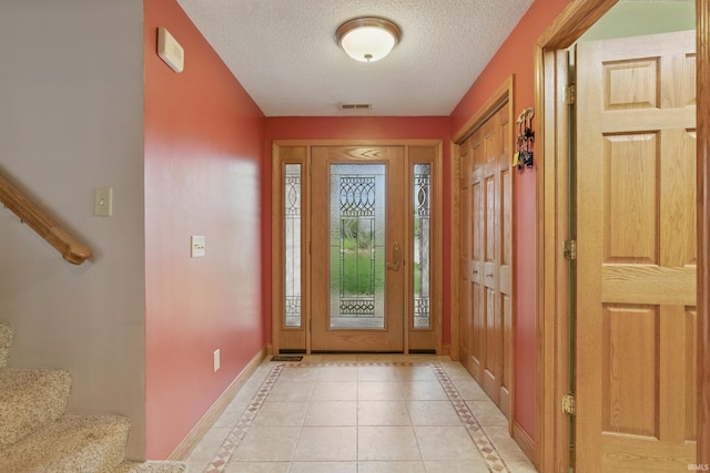 entryway with inlaid floor details, baseboards, stairway, a textured ceiling, and light tile patterned floors