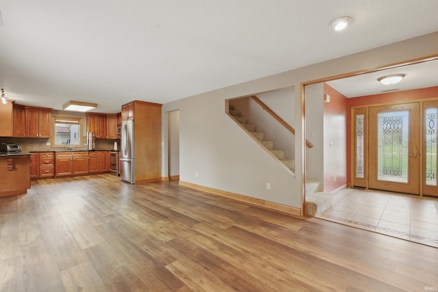 kitchen with appliances with stainless steel finishes, light wood-style flooring, brown cabinets, tasteful backsplash, and baseboards