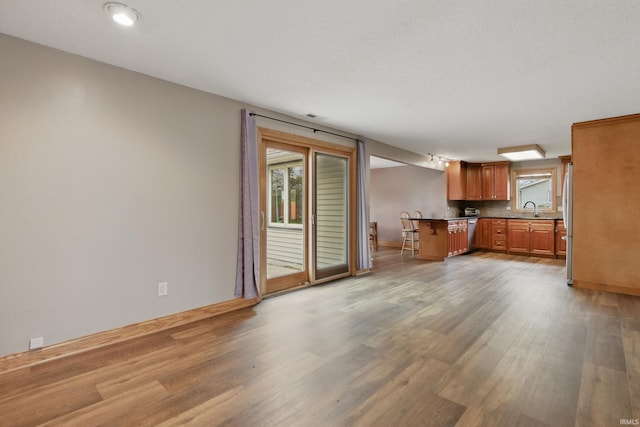 unfurnished living room with a sink, wood finished floors, and baseboards