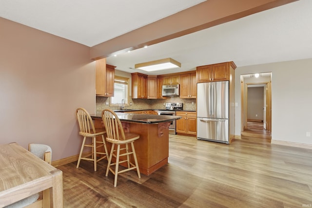kitchen featuring appliances with stainless steel finishes, dark countertops, light wood-style flooring, tasteful backsplash, and a peninsula