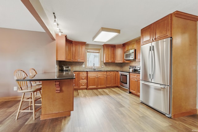 kitchen with stainless steel appliances, a peninsula, a sink, and light wood-style flooring