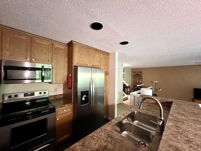 kitchen featuring stainless steel appliances, a sink, a textured ceiling, and brown cabinets