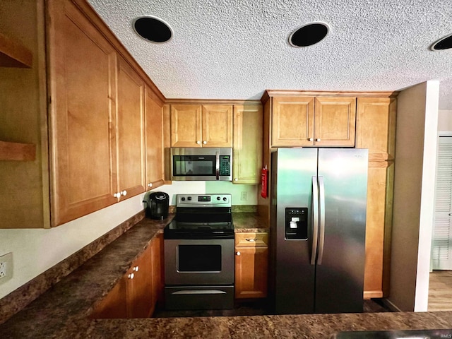 kitchen with appliances with stainless steel finishes, dark countertops, brown cabinets, and a textured ceiling