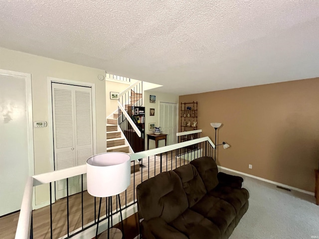 living area featuring a textured ceiling, stairs, baseboards, and carpet floors