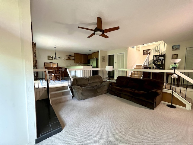 living area featuring a ceiling fan, stairs, carpet floors, and a chandelier