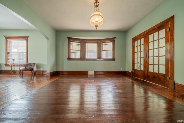 spare room featuring wood-type flooring, arched walkways, french doors, and baseboards
