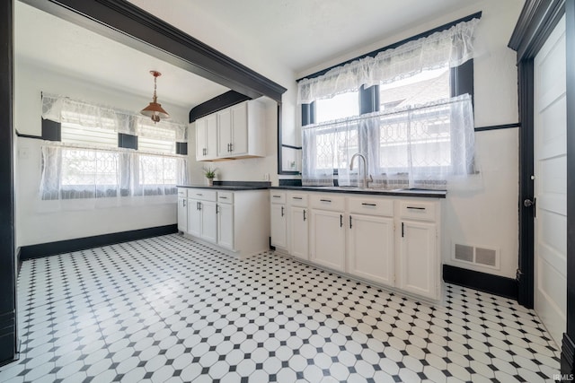 kitchen featuring dark countertops, white cabinets, baseboards, and a sink