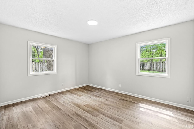 unfurnished room with plenty of natural light, wood finished floors, baseboards, and a textured ceiling