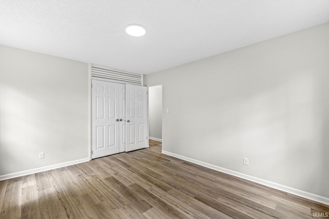 unfurnished bedroom featuring wood finished floors, baseboards, and a closet