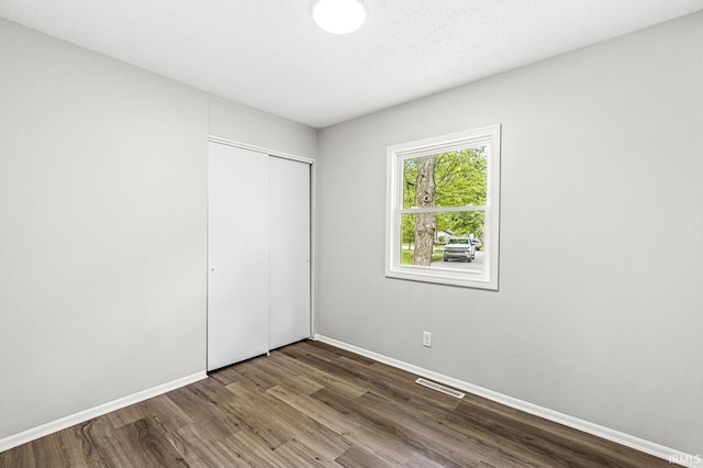 unfurnished bedroom with dark wood-style floors, baseboards, and a closet