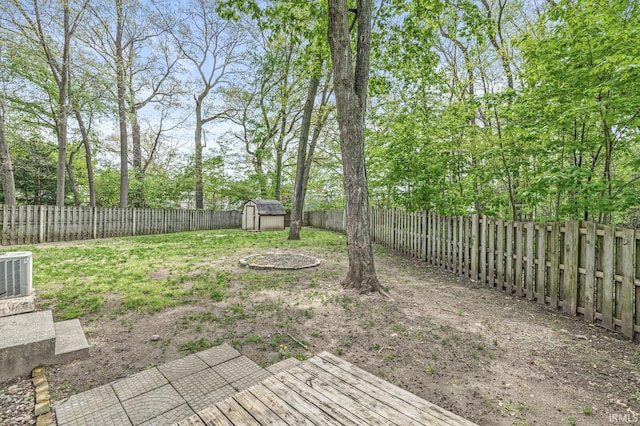 fenced backyard with a shed, an outbuilding, central AC, and view of scattered trees