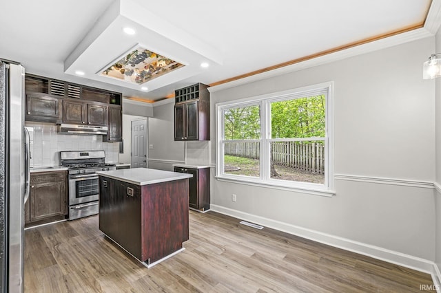 kitchen with appliances with stainless steel finishes, under cabinet range hood, light countertops, baseboards, and a center island
