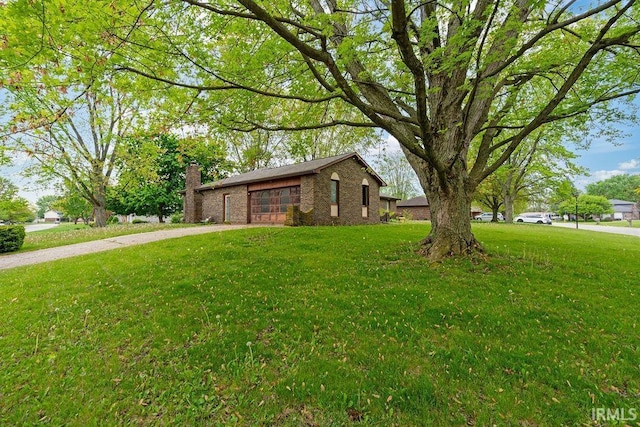 view of front of house with driveway, brick siding, a garage, a front lawn, and a chimney