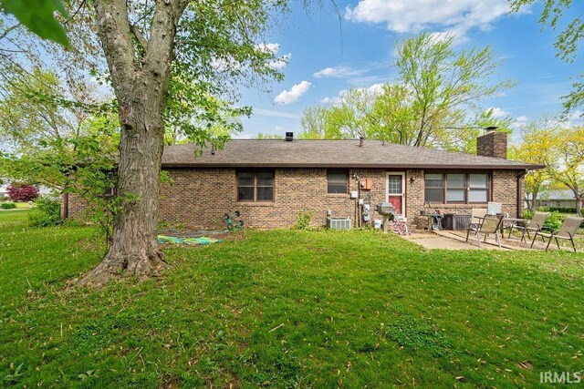 back of property featuring a patio, a chimney, brick siding, a lawn, and central AC