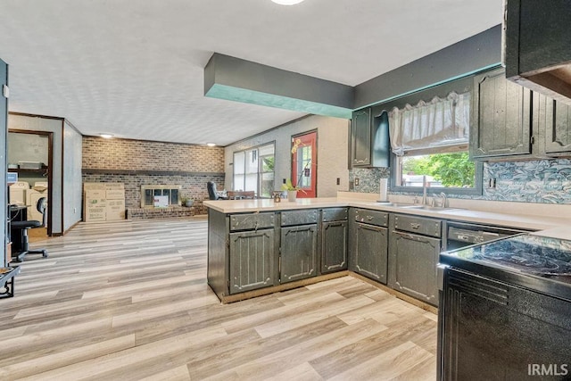 kitchen featuring a peninsula, a sink, light countertops, light wood-style flooring, and a fireplace