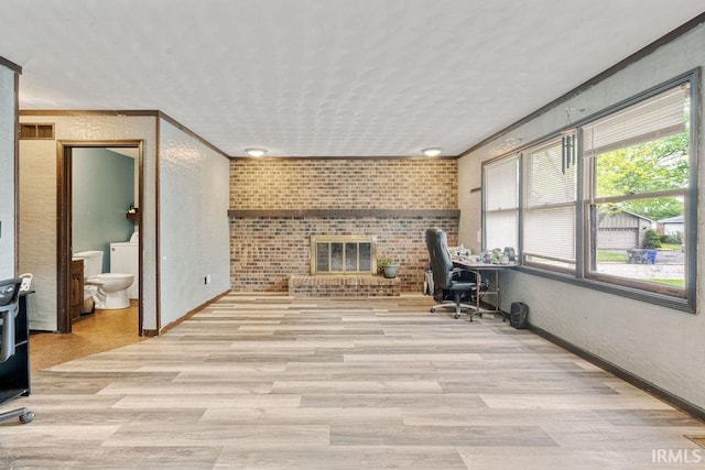 office with baseboards, light wood-style flooring, brick wall, a brick fireplace, and a textured ceiling