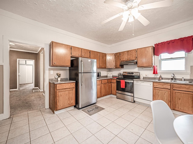 kitchen with appliances with stainless steel finishes, under cabinet range hood, a sink, brown cabinetry, and a textured ceiling