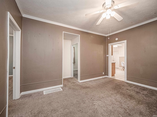 unfurnished bedroom featuring carpet, ensuite bathroom, ornamental molding, baseboards, and a ceiling fan