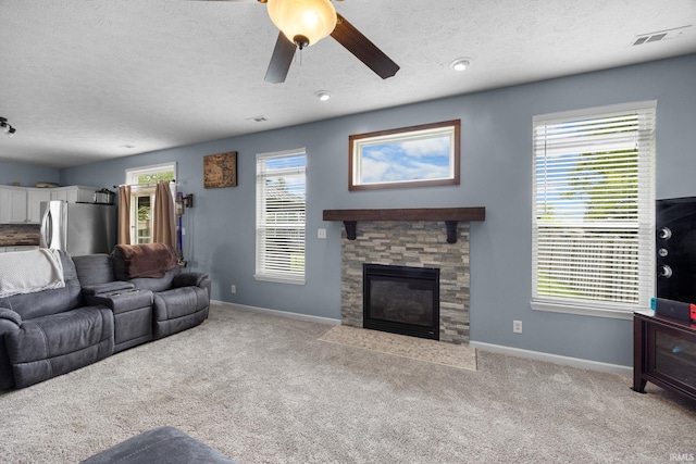 living area with a textured ceiling, baseboards, a stone fireplace, carpet, and a ceiling fan