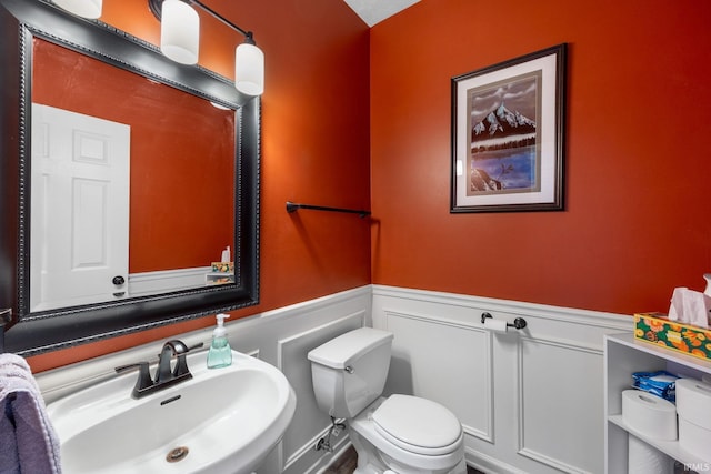 bathroom featuring a sink, wainscoting, toilet, and a decorative wall