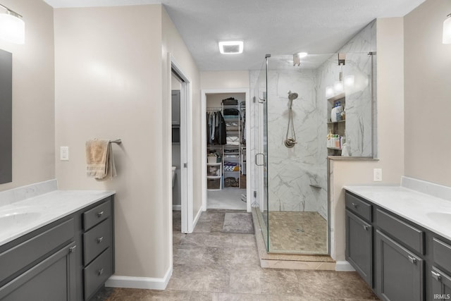bathroom featuring a marble finish shower, two vanities, a walk in closet, and baseboards