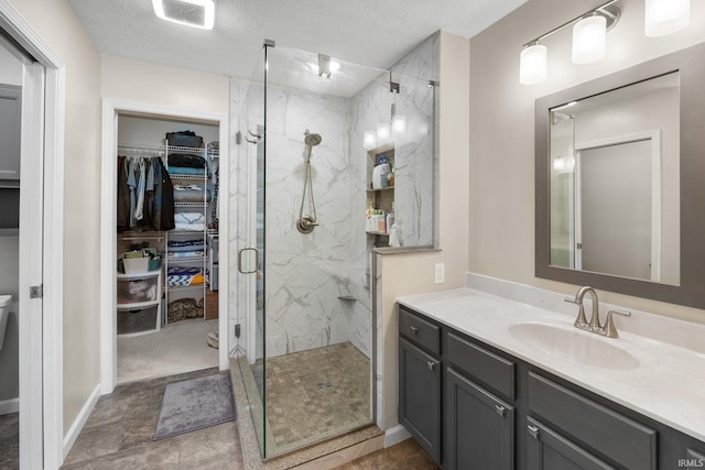 bathroom with a marble finish shower, a walk in closet, vanity, and a textured ceiling