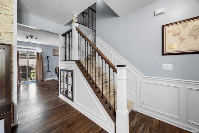 staircase featuring a textured ceiling, a decorative wall, wood finished floors, and a wainscoted wall