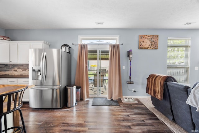kitchen featuring stainless steel fridge, dark wood-type flooring, white cabinets, dark countertops, and backsplash