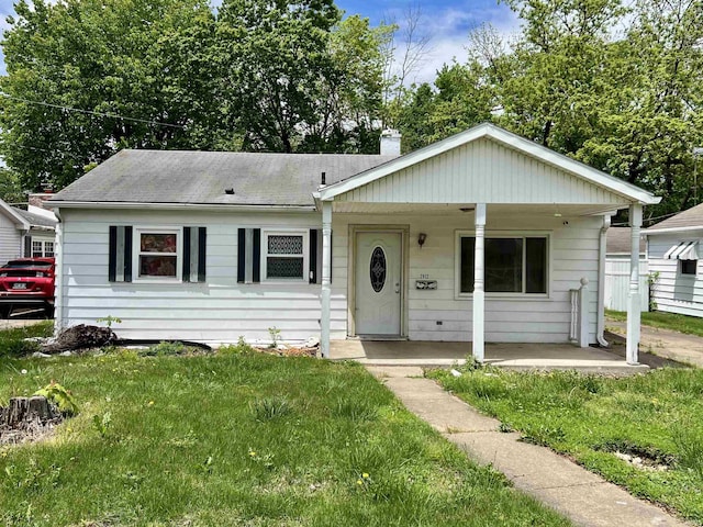 view of front of home featuring a chimney, a porch, a front yard, and a shingled roof