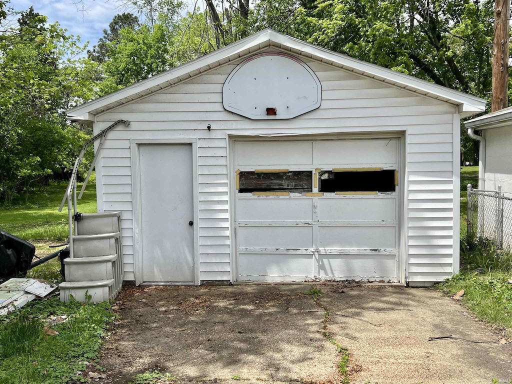 detached garage featuring driveway, fence, and view of wooded area