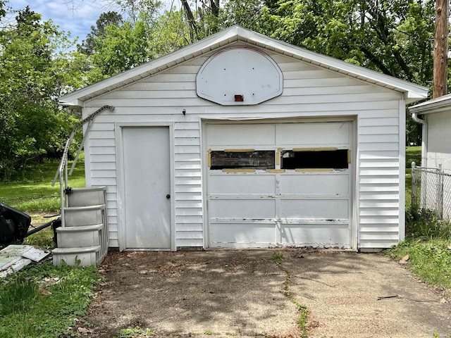 detached garage featuring driveway, fence, and view of wooded area