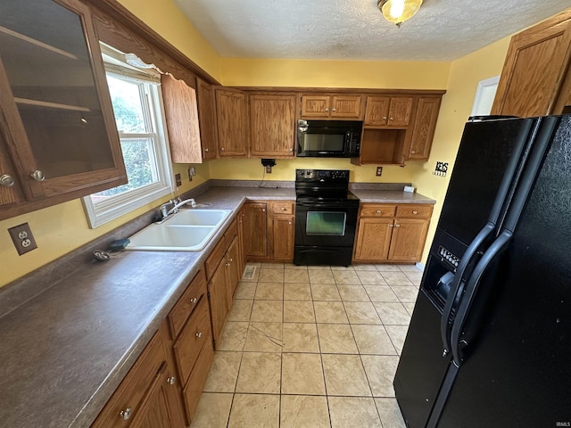 kitchen featuring black appliances, a sink, brown cabinetry, a textured ceiling, and light tile patterned floors