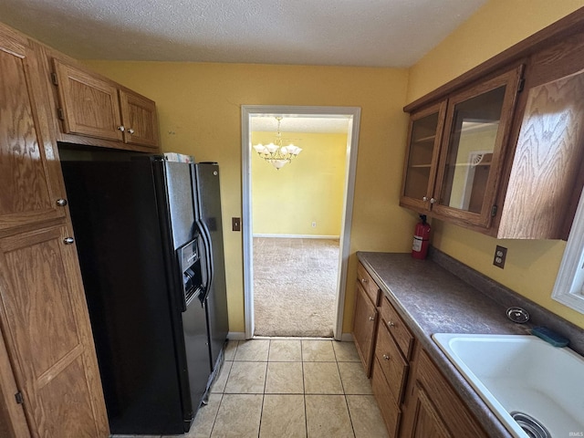 kitchen featuring black refrigerator with ice dispenser, a sink, brown cabinets, a chandelier, and glass insert cabinets