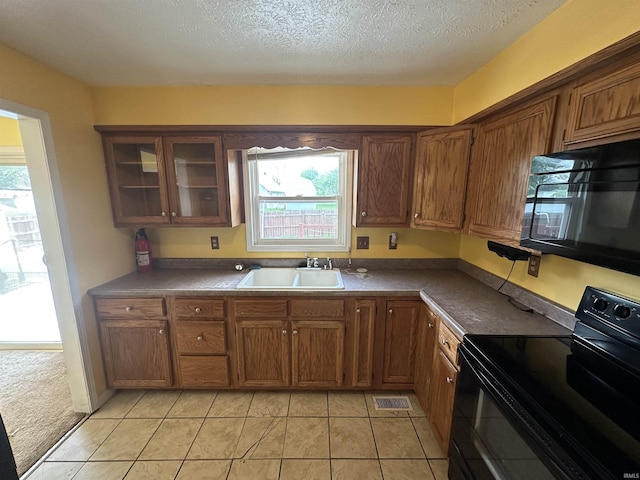 kitchen featuring black appliances, a sink, healthy amount of natural light, a textured ceiling, and brown cabinetry