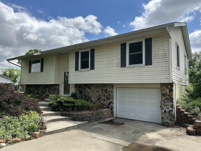 split foyer home featuring stone siding, an attached garage, and concrete driveway
