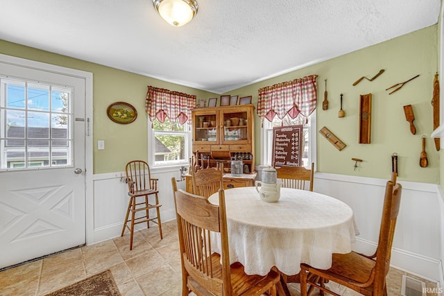 dining area featuring wainscoting, a textured ceiling, and a decorative wall