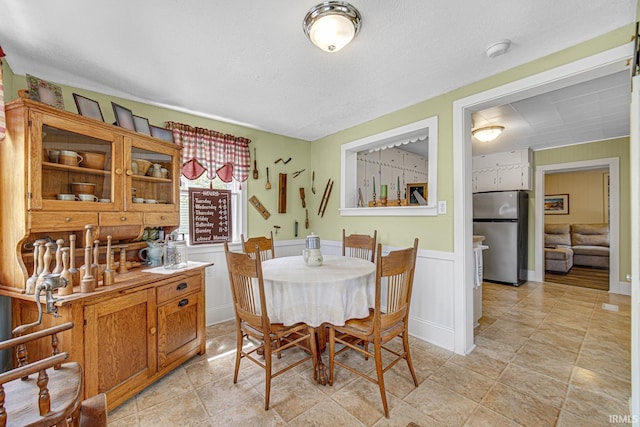 dining room with a textured ceiling, a wainscoted wall, and a decorative wall