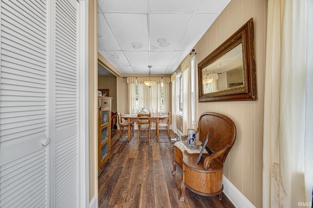 hall featuring dark wood-type flooring, a drop ceiling, and baseboards