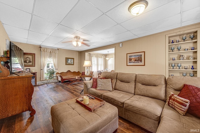 living room featuring dark wood-style flooring, a drop ceiling, ceiling fan, and built in features