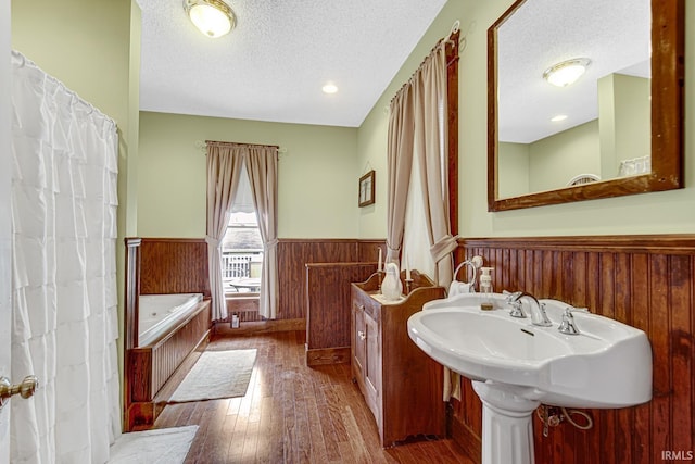 full bathroom featuring wainscoting, a textured ceiling, hardwood / wood-style floors, and a bath