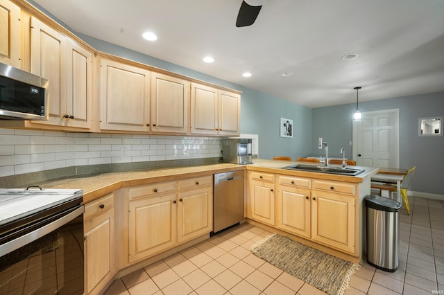 kitchen featuring stainless steel appliances, a sink, a peninsula, light brown cabinets, and decorative backsplash