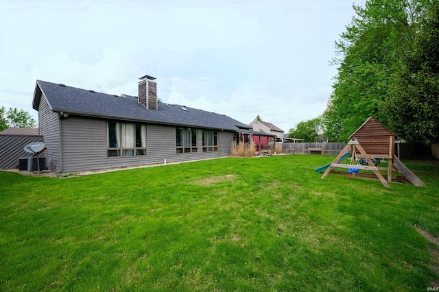back of house with a chimney, cooling unit, and roof with shingles