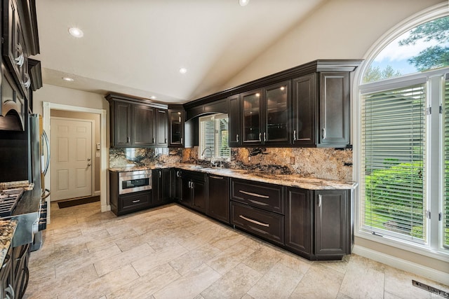 51167 Huntington Ln, Granger, IN 46530 - kitchen featuring lofted ceiling, a sink, decorative backsplash, light stone countertops, and arched walkways