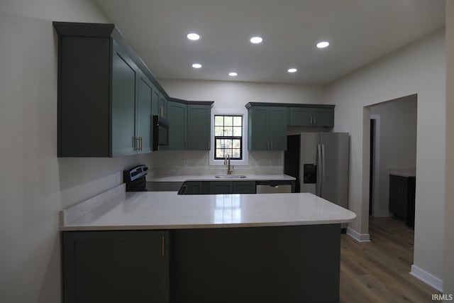 kitchen featuring appliances with stainless steel finishes, a sink, a peninsula, light wood finished floors, and recessed lighting