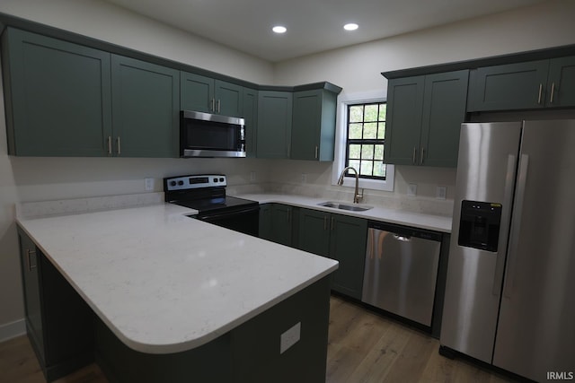 kitchen featuring stainless steel appliances, a sink, a peninsula, light wood-type flooring, and recessed lighting