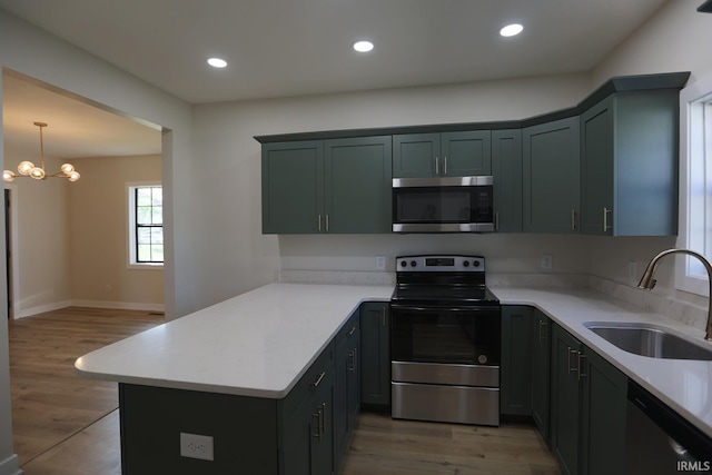 kitchen featuring stainless steel appliances, a sink, a peninsula, light wood finished floors, and recessed lighting