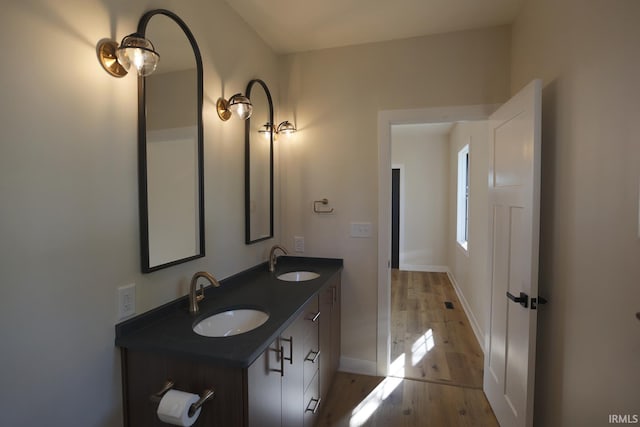 bathroom featuring baseboards, wood finished floors, and double vanity